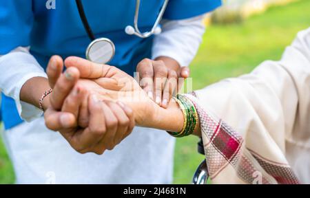 Nahaufnahme des Arztes, der die Pulsfrequenz der Frau überprüft, indem er die Hand in den Park hält - Konzept der medizinischen Behandlung oder Gesundheitsfürsorge und Berufstätigkeit Stockfoto