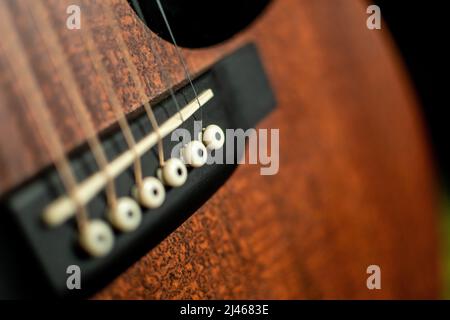 Eine selektive Nahaufnahme der Brücke einer akustischen Gitarre mit Sattel, Steg Pins und Stahlsaiten. Stockfoto