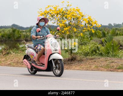 SAMUT PRAKAN, THAILAND, MÄRZ 23 2022, Eine Frau mit Hut reitet auf einem rosa Moped Stockfoto