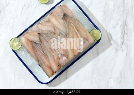 Rohe Filet von gefrorenen weißen Fischwelsen auf einem weißen Emaille-Tablett, weißer Hintergrund. Draufsicht Stockfoto