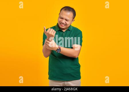 Porträt eines asiatischen jungen Mannes, der an Schmerzen in Händen und Fingern auf gelbem Hintergrund leidet Stockfoto