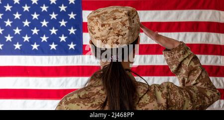 Soldatinnen der US-Armee, die vor einer amerikanischen Flagge steht und grüsst. Frau in Militäruniform Rückansicht Stockfoto
