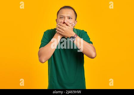 Überrascht junge asiatische Frau bedeckt Mund mit Hand auf gelbem Hintergrund Stockfoto