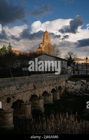 Katholische Kirche - Parroquia de la Asuncion de Nuestra Senora - in Venialbo, in der Nähe von Zamora, Spanien. Gesehen über der alten Steinbrücke über Arroyo Talanda Stockfoto