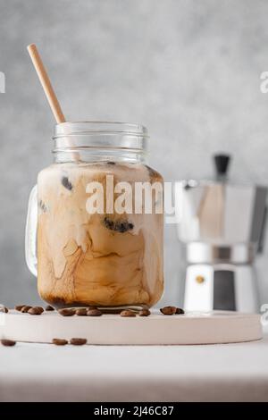 Eiskaffee mit Milch oder Rahm in einem Glasgefäß mit Stroh auf grauem Hintergrund. Kalte Erfrischung Sommergetränk. Vertikale Ausrichtung Stockfoto