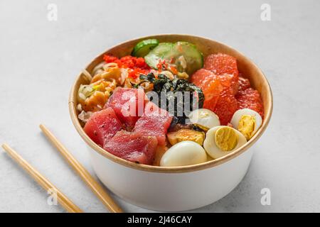 Thunfisch-Poke-Schüssel-Salat in Papierverpackung mit Essstäbchen zum Mitnehmen oder zur Lebensmittelzustellung auf weißem Hintergrund. Gesunde Ernährung Stockfoto