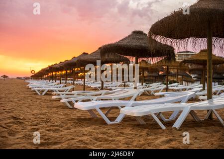 Schöner, farbenfroher Sonnenuntergang über Liegestühlen und Sonnenschirmen in Vilamoura, Algarve, Portugal Stockfoto