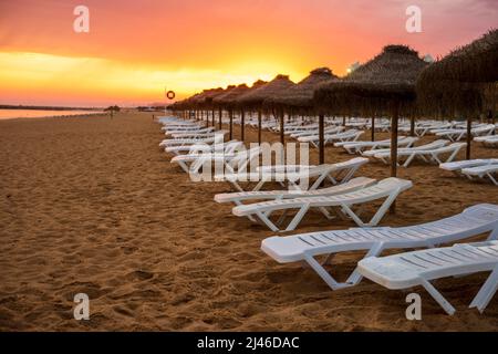 Schöner, farbenfroher Sonnenuntergang über Liegestühlen und Sonnenschirmen in Vilamoura, Algarve, Portugal Stockfoto