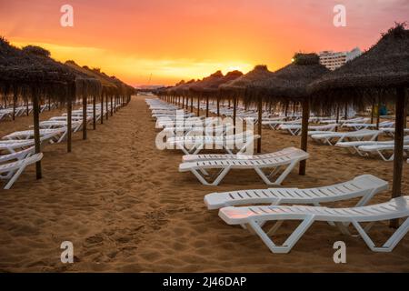 Schöner, farbenfroher Sonnenuntergang über Liegestühlen und Sonnenschirmen in Vilamoura, Algarve, Portugal Stockfoto