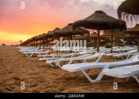 Schöner, farbenfroher Sonnenuntergang über Liegestühlen und Sonnenschirmen in Vilamoura, Algarve, Portugal Stockfoto