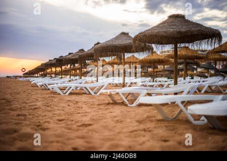 Schöner, farbenfroher Sonnenuntergang über Liegestühlen und Sonnenschirmen in Vilamoura, Algarve, Portugal Stockfoto