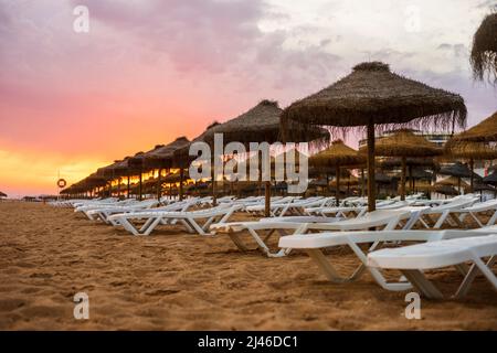 Schöner, farbenfroher Sonnenuntergang über Liegestühlen und Sonnenschirmen in Vilamoura, Algarve, Portugal Stockfoto