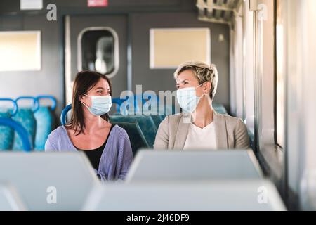 Ein paar Freunde tragen eine Maske und unterhalten sich während der Reise mit dem Zug Stockfoto