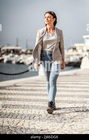 Ein Porträt einer jungen selbstbewussten Frau, die am Yachthafen durch die Stadt läuft Stockfoto