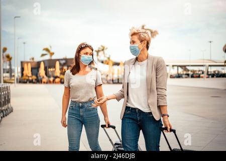 Reisende Frauen in Schutzmasken reden beim Verlassen des Flughafens am Zielort Stockfoto