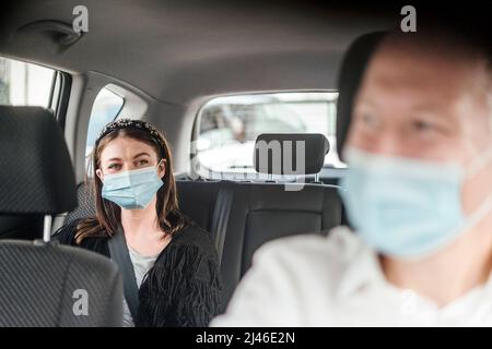 Eine Frau, die eine Schutzmaske trägt und auf dem Rücksitz eines Taxiwagens sitzt Stockfoto