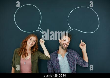 Sich Gehör verschaffen. Porträt eines jungen Paares, das vor einer Tafel steht, auf der Sprechblasen gezeichnet sind. Stockfoto