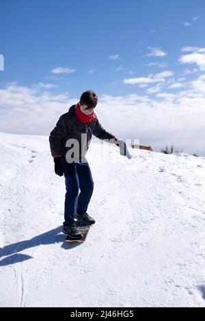 Fröhlicher Teenager-Mann reiten Board auf Schneehügel an klaren frostigen Tag. Stockfoto