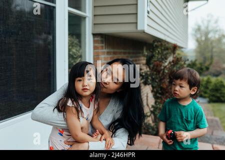 Mutter sitzt auf der Veranda mit Tochter im Schoß und Sohn in der Nähe Stockfoto
