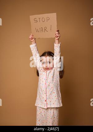 Studio-Aufnahme eines entzückenden verärgert 4 Jahre altes Kind, traurige kleine europäische Mädchen in Pyjamas mit Stop war Social Message Karton Poster stehend auf bei Stockfoto