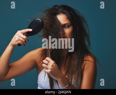 Es ist nicht nur eine Frisur, es ist ein Geisteszustand. Studioaufnahme einer schönen jungen Frau, die einen Pinsel an ihr Haar hält und vor blauem Hintergrund posiert. Stockfoto