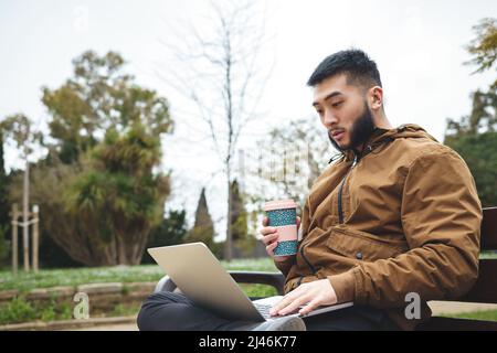 Seriöser ethnischer Freiberufler, der an einem Laptop arbeitet und Kaffee trinkt Stockfoto