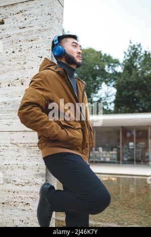Ethnischer Mann, der Musik hört, während er sich an die Wand lehnt Stockfoto