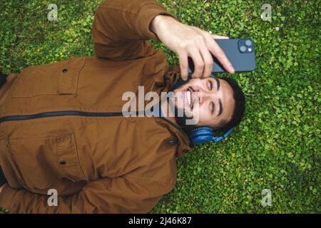 Fröhlicher ethnischer Mann mit Kopfhörern, der Selfie auf dem Smartphone nimmt Stockfoto