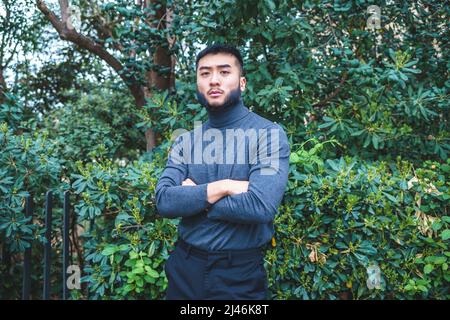 Selbstbewusster ethnischer Mann, der in der Nähe von grünen Büschen im Park steht Stockfoto