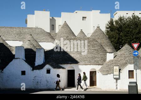 Menschen, die an den 500 Jahre alten traditionellen Trulli-Steinhäusern in Alberobello, Italien, vorbeikommen Stockfoto