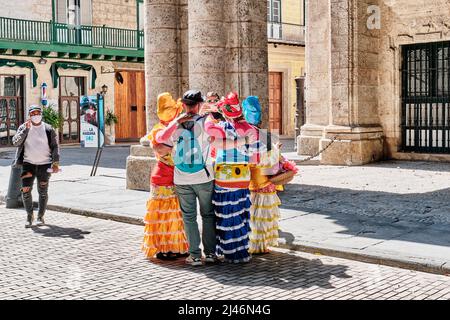Touristen fotografieren mit lokalen kubanischen Frauen in traditionellen bunten Kleidern in der Altstadt von Havanna, Kuba Stockfoto