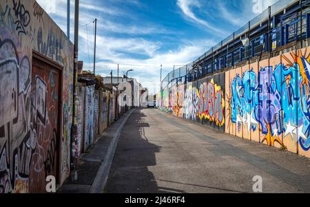 Eine kleine Gasse hinter dem Fußballstadion des FC Portsmouth namens Fratton Park mit Wänden, die mit farbenfrohen Graffiti bedeckt sind. Stockfoto