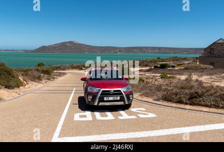 Langabaan, Westküste, Südafrika. 2022. Rotes Auto nähert sich einem Stoppschild auf der Küstenstraße in Langabaan mit der Westküste Nationa über das Meer Stockfoto