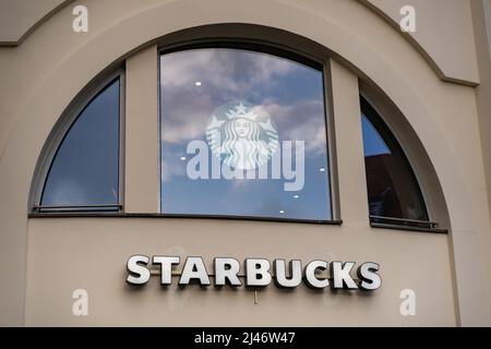 Starbucks-Buchstaben und das Logo als Teil der Fassade eines Gebäudes in der Stadt. Werbung für das berühmte Kaffeeunternehmen, das ein Franchise betreibt Stockfoto