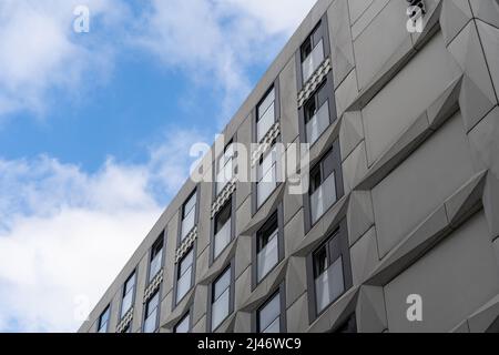 Modernes Fassadendesign vor einem blauen Himmel mit weißen Wolken. Graue Elemente mit Relief und Glasfenstern. Futuristische Architektur im Außenbereich. Stockfoto