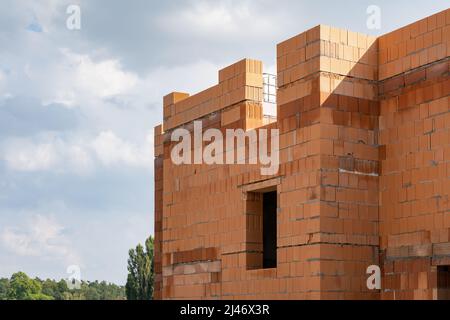 Eine Baustelle mit einem Haus aus roten Ziegeln. Die façade ist nicht überdacht und das Gebäude hat noch kein Dach. Das Haus ist in Arbeit. Stockfoto