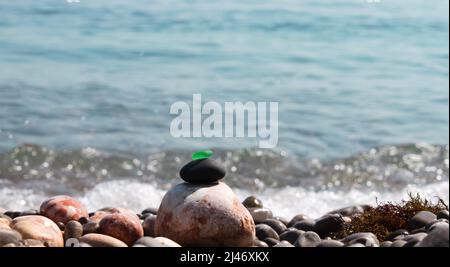 Die Pyramide ist auf einem Kiesstrand aus Kieselsteinen mit einem matten, glatten, grünen Glas an der Spitze gebaut. Vor dem Hintergrund von Wellen, Wasserspritzern und Stockfoto