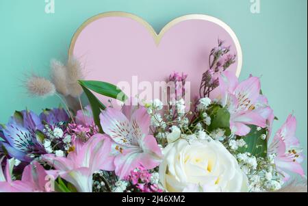 Zartes Bouquet von rosa Lilien, weißen Rosen, Gypsophila. Türkisfarbener Hintergrund. Rosafarbenes Herz, Kopierbereich. Stockfoto
