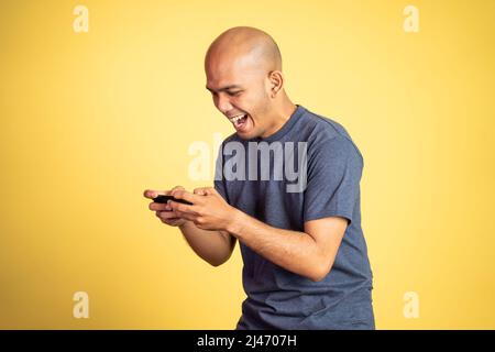 Kahlköpfiger asiatischer Mann lacht beim Spielen mit dem Smartphone Stockfoto
