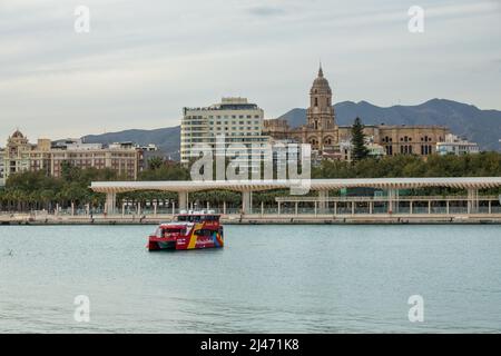 Málaga, Spanien; 02. April 2022: Blick auf den Pier in Malaga (Spanien) mit einem roten Boot für touristische Tour und dem Glockenturm der Kathedrale im Hintergrund Stockfoto