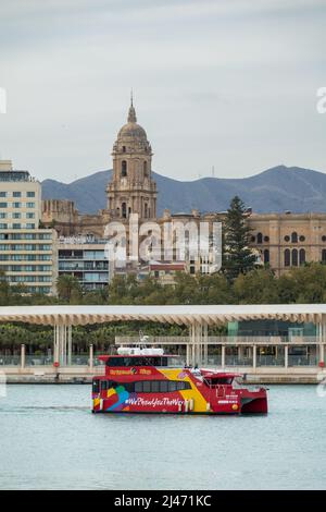 Málaga, Spanien; 02. April 2022: Blick auf den Pier in Malaga (Spanien) mit einem roten Boot für touristische Tour und dem Glockenturm der Kathedrale im Hintergrund Stockfoto