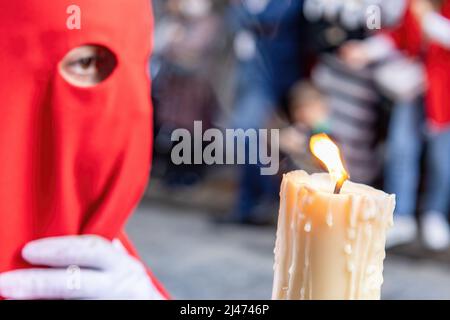 Die brennende Kerze eines jungen Nazareners mit einer roten Kapuze, der in der Karwoche seine Buße tat. Selektiver Fokus nur mit Kerzenflamme Stockfoto