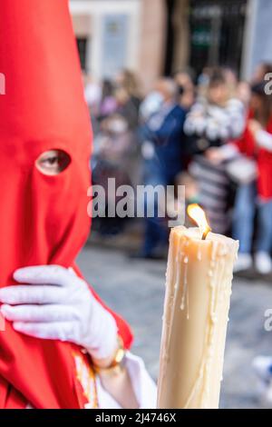 Die brennende Kerze eines jungen Nazareners mit einer roten Kapuze, der in der Karwoche seine Buße tat. Selektiver Fokus nur mit Kerzenflamme Stockfoto