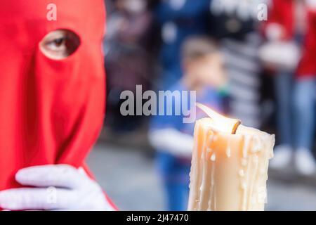 Die brennende Kerze eines jungen Nazareners mit einer roten Kapuze, der in der Karwoche seine Buße tat. Selektiver Fokus nur mit Kerzenflamme Stockfoto