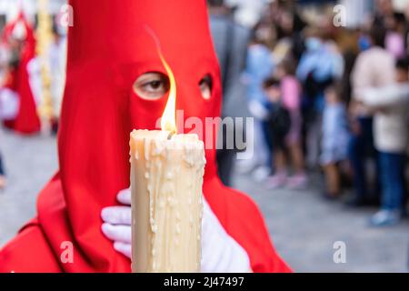 Die brennende Kerze eines jungen Nazareners mit einer roten Kapuze, der in der Karwoche seine Buße tat. Selektiver Fokus nur mit Kerzenflamme Stockfoto