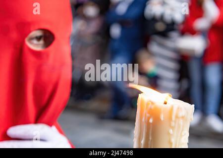 Die brennende Kerze eines jungen Nazareners mit einer roten Kapuze, der in der Karwoche seine Buße tat. Selektiver Fokus nur mit Kerzenflamme Stockfoto