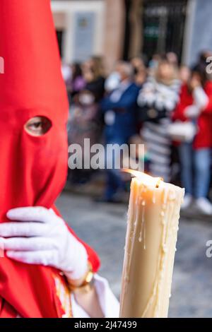 Die brennende Kerze eines jungen Nazareners mit einer roten Kapuze, der in der Karwoche seine Buße tat. Selektiver Fokus nur mit Kerzenflamme Stockfoto