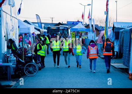 Przemysl, Polen. 12. April 2022. Am Grenzübergang Medyka, direkt über die ukrainische Grenze auf polnischer Seite, laufen am Abend Freiwillige zwischen den Zelten von Hilfsorganisationen, wobei kaum Flüchtlinge unterwegs sind. Quelle: Christoph Soeder/dpa/Alamy Live News Stockfoto