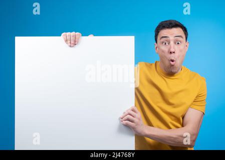 Schockierter Mann, der im Studio ein leeres Banner zeigt Stockfoto