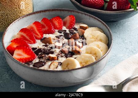 Hirsebrei mit Erdbeere, Banane, dunklen Schokoladenstücken, Haselnuss und Mandel in einer Keramikschale Stockfoto
